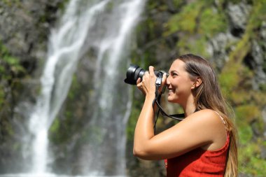 Side view portrait of a happy woman taking photos with mirrorless camera in nature clipart