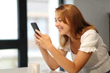 Evde akıllı telefondan mesaj okuyan mutlu kadın.