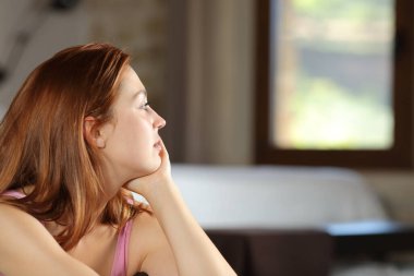 Dikkati dağılmış bir kadın yatak odasının penceresinden bakıyor.