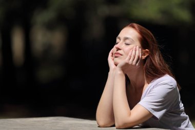 Kapalı gözlü kadın güneşli bir günde parkta dinleniyor ve ısınıyor.