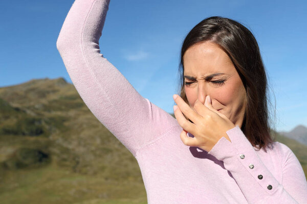 Casual woman smelling stinky underarm in the mountain a warm day