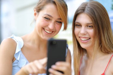 İki mutlu arkadaş akıllı telefon kullanıyor ve sokakta gülüyor.