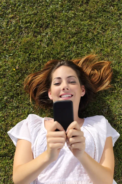Bovenaanzicht van een vrouw liggend op de SMS gras op een slimme telefoon — Stockfoto