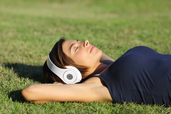 Relaxed woman listening to the music with headphones lying on the grass — Stock Photo, Image