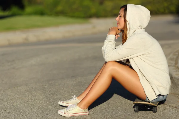 Perfil de uma adolescente pensativa sentada em um skate na rua — Fotografia de Stock