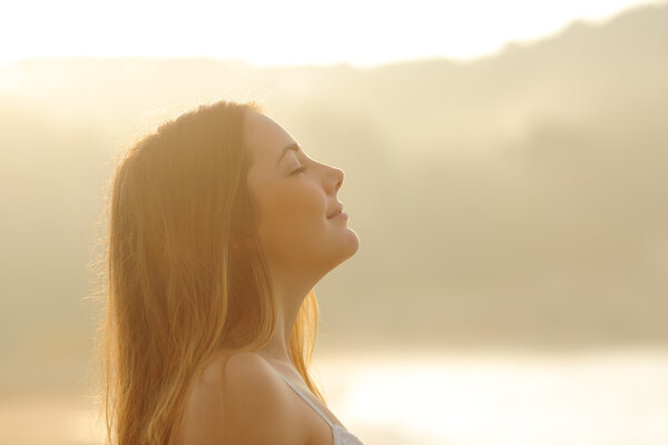 Woman breathing deep fresh air in the morning sunrise