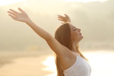 Relaxed woman breathing fresh air raising arms at sunrise clipart