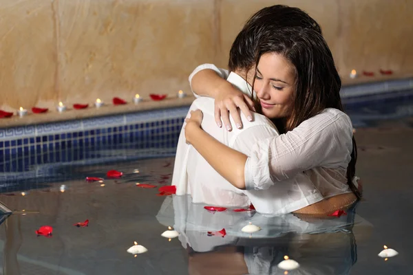 Romantic couple hugging in a pool  with candles and rose petals — Stock Photo, Image