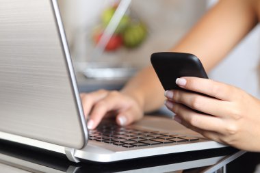 Bir akıllı telefon kullanarak ve bir dizüstü bilgisayar evde yazarak kadın el
