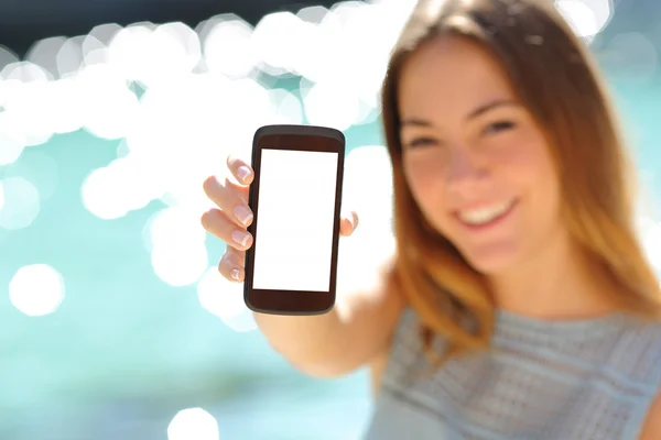 Mulher feliz mostrando um smartphone em branco na praia — Fotografia de Stock