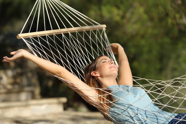 Mulher feliz relaxando em uma rede em férias e levantando braços — Fotografia de Stock