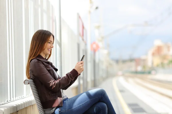 Bir tren istasyonunda bir akıllı telefon üzerinde mutlu kadın manifatura — Stok fotoğraf