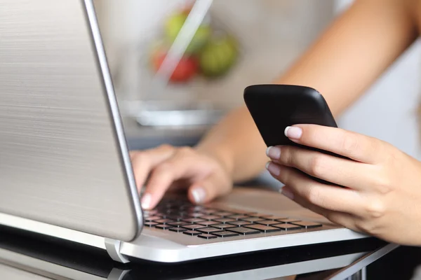 Mujer mano usando un teléfono inteligente y escribiendo una computadora portátil en casa — Foto de Stock