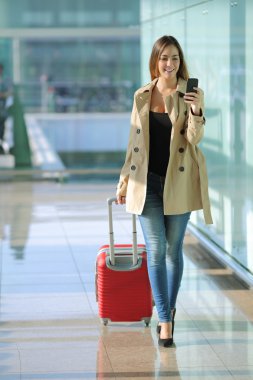 Traveler woman walking and using a smart phone in an airport clipart