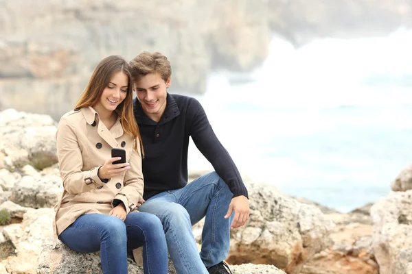 Coppia che condivide uno smartphone in spiaggia in vacanza — Foto Stock