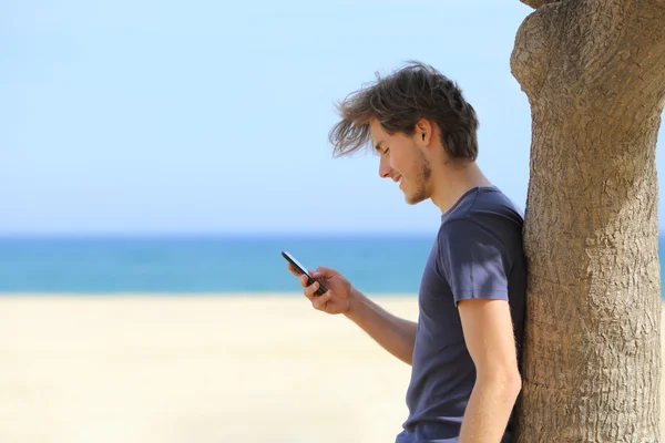 Sidovy av en attraktiv man använder en smart telefon på stranden — Stockfoto
