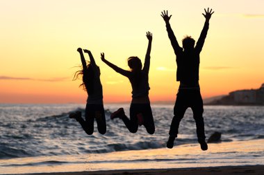 Friends silhouette jumping happy on the beach at sunset clipart