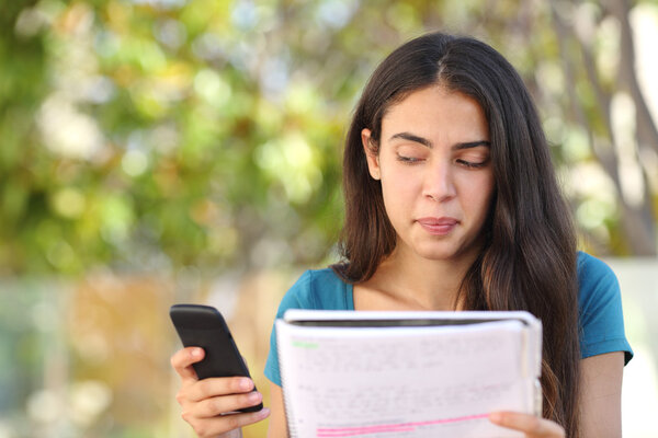Teenager student girl looking sideways at mobile phone while studying