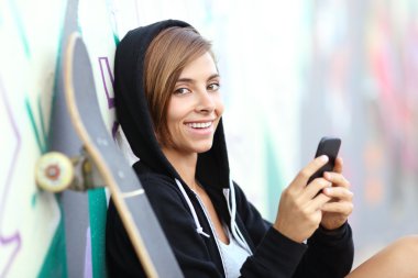 Kameraya bakarak bir akıllı telefon kullanan genç kaykaycı kız