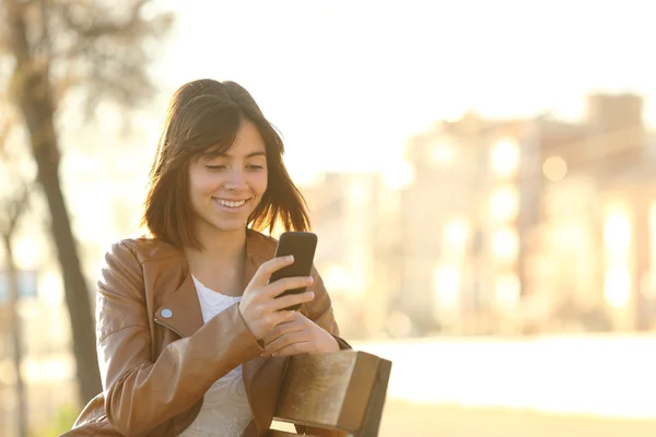 Fille heureuse utilisant un téléphone intelligent dans un parc de la ville — Photo