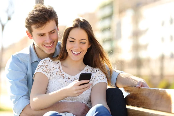 Çift bir parkta bir akıllı telefon medya paylaşımı — Stok fotoğraf