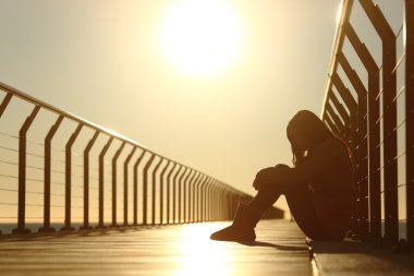 Bir köprü günbatımında oturan depresif üzgün genç kız