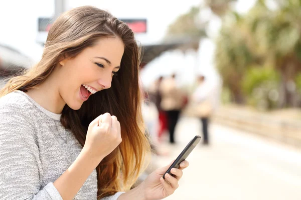 Mujer eufórica mirando su teléfono inteligente en una estación de tren —  Fotos de Stock