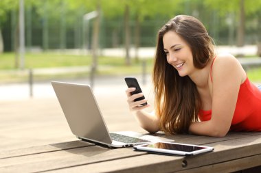 Bir dizüstü bilgisayar ve akıllı telefon kullanan bir parkta kız