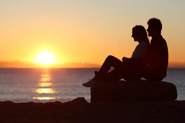 Пара силуэтов сидят и смотрят на солнце на закате — стоковое фото