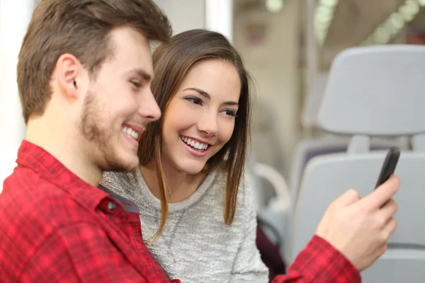 Un par de pasajeros compartiendo un teléfono inteligente dentro de un tren — Foto de Stock