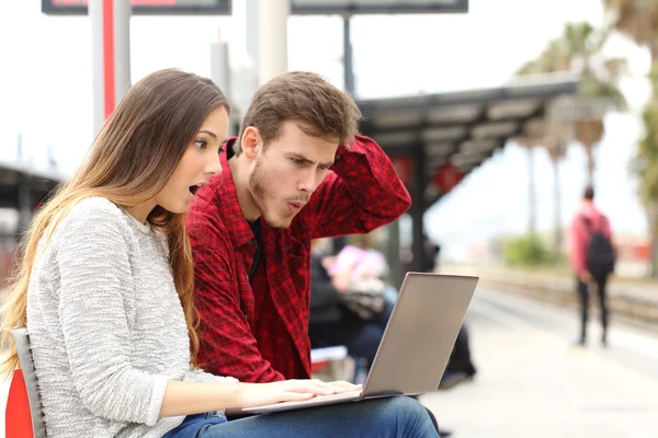 Casal surpreendido assistindo um laptop em uma estação de trem — Fotografia de Stock