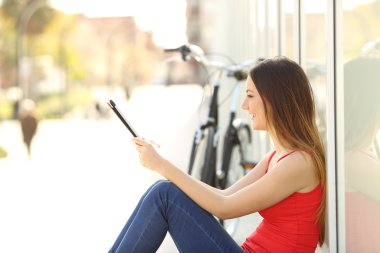 Genç kız sokakta oturan bir tablet kullanma