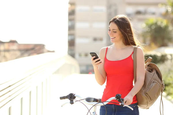 Mulher usando um telefone inteligente andando com uma bicicleta — Fotografia de Stock