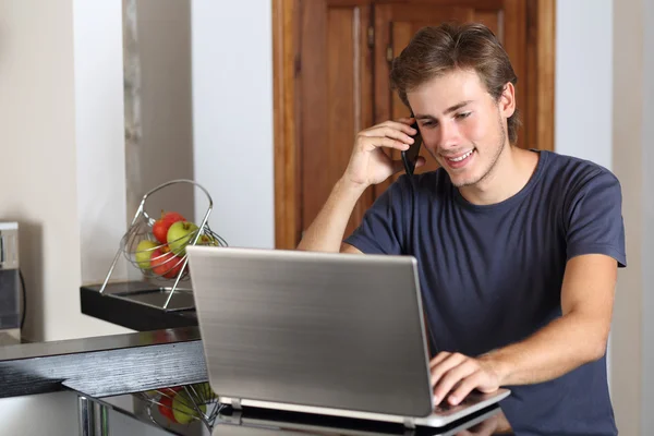 Muž na telefonu, pracující s přenosným počítačem doma — Stock fotografie
