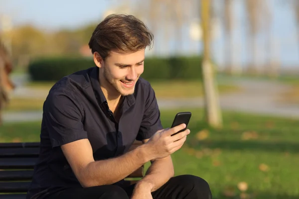 Hombre usando un teléfono inteligente sentado en un banco en un parque — Foto de Stock