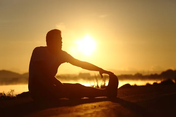 Silhouette of a fitness man stretching at sunset — Stock Photo, Image