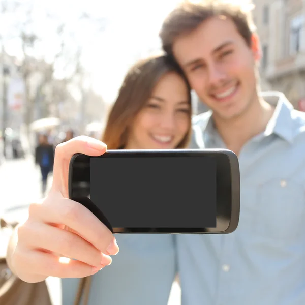 Casal fazendo uma foto selfie com um smartphone e mostrando tela — Fotografia de Stock