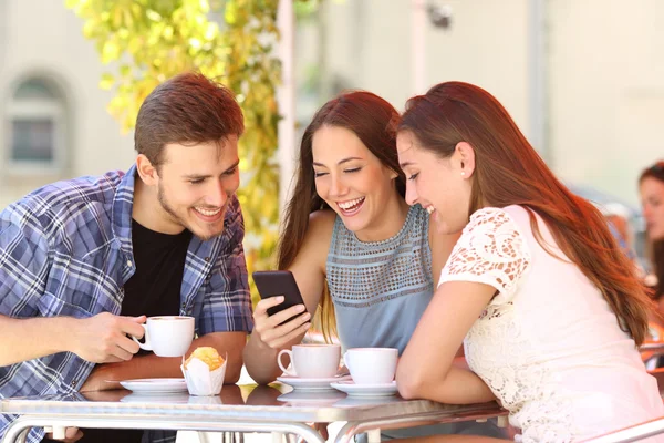 Vrienden kijken van de media in een slimme telefoon in een koffieshop Stockfoto