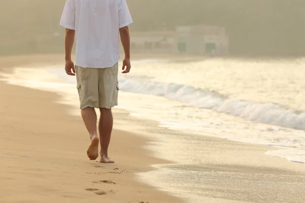Человек ходит и оставляет следы на песке на пляже — стоковое фото