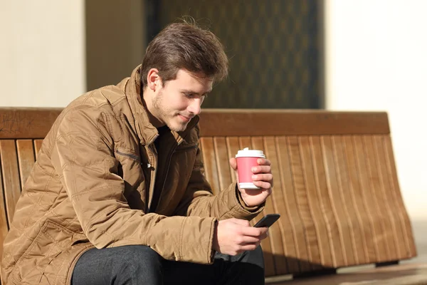 Homem usando um telefone inteligente e segurando uma xícara de café — Fotografia de Stock