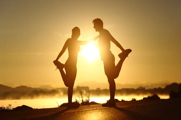 Silhueta de um par de fitness que se estende ao pôr do sol — Fotografia de Stock