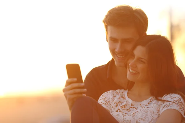 Luz traseira de um casal compartilhando um telefone inteligente — Fotografia de Stock