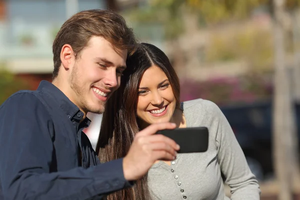 Lyckliga paret tittar på media i en smart telefon utomhus — Stockfoto