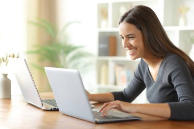 Mutlu kadın aynı anda iki dizüstü bilgisayar kullanıyor. Evdeki ahşap masada.