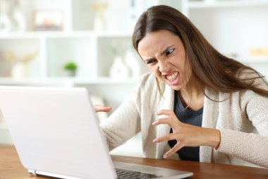 Kızgın kadın evin içinde dizüstü bilgisayar içeriğini kontrol ediyor.