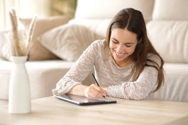 Evin içindeki bir sehpanın üzerindeki dijital tablette mutlu kadın el yazısı