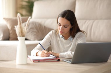 Öğrenci evde dizüstü bilgisayarın yanında not alıyor.