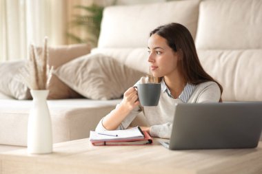 Kahve içen ve ara veren bir öğrenci dikkati dağılmış bir şekilde evdeki oturma odasına bakıyor.