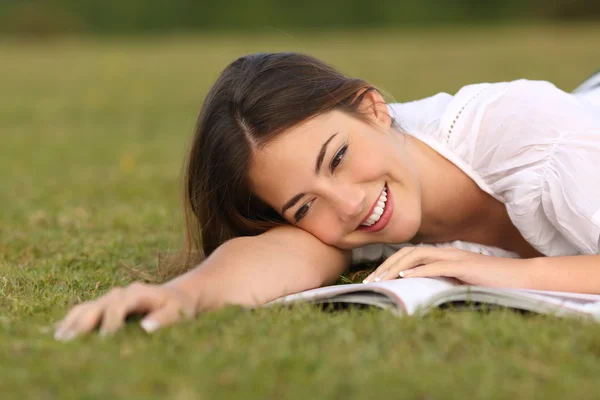 Schöne Frau, die im Gras liegt und ein Papierbuch liest — Stockfoto