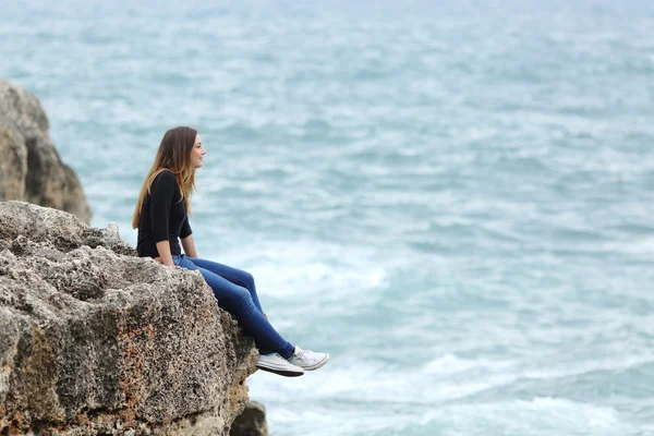 Mujer casual sentada en un acantilado mirando el mar — Foto de Stock